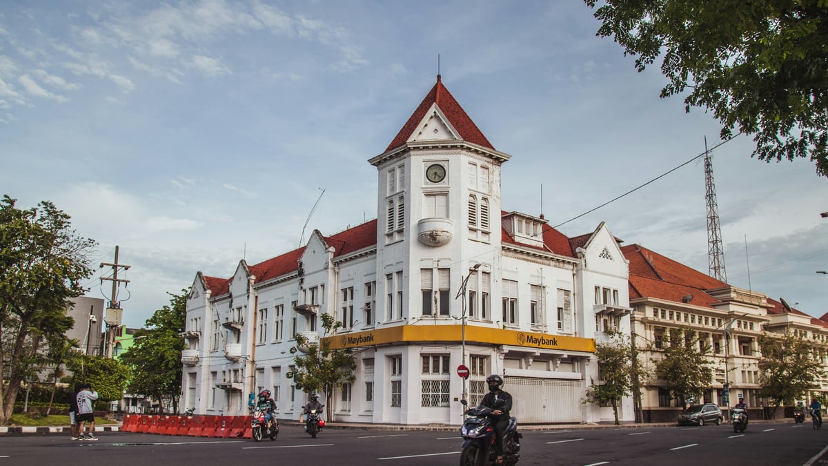 A white heritage building on a Surabaya street with a motorcyclist passing by, representing the city's trading history