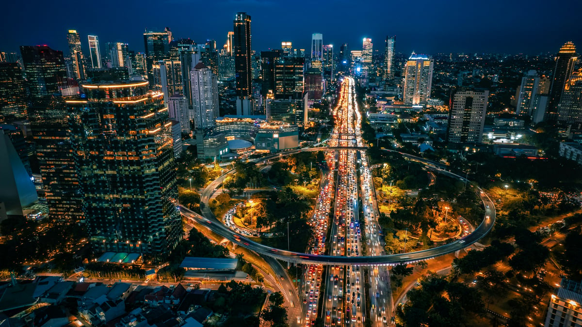 Pemandangan udara Jakarta pada malam hari dengan jejak lampu lalu lintas, mencerminkan aktivitas bisnis dan teknologi kota ini
