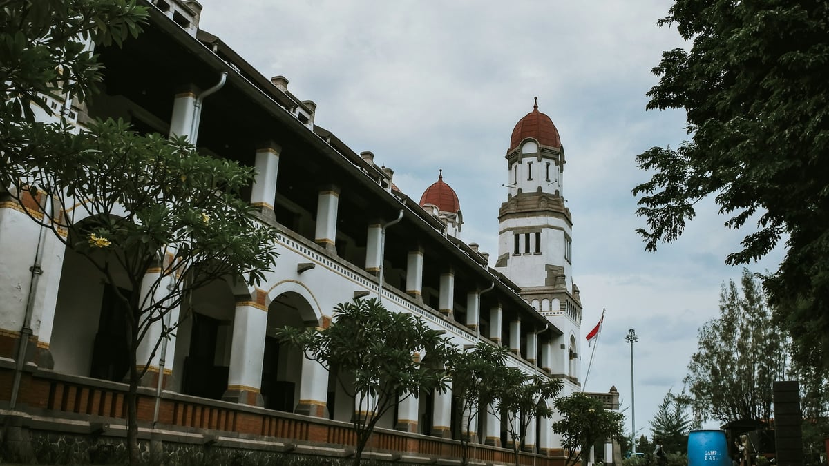 Bangunan putih bersejarah dengan lorong berpilar lengkung dan menara jam di Semarang di bawah langit berawan